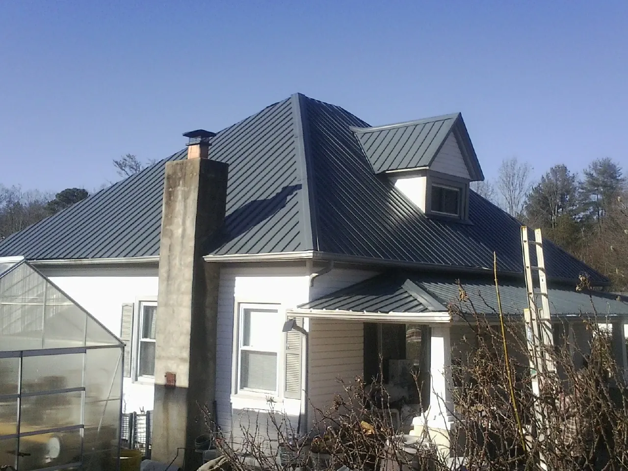 Dark blue standing seam metal roof on a white farmhouse with dormer — Slate & Tile Roof Repair by Roofing Brothers in Outlook