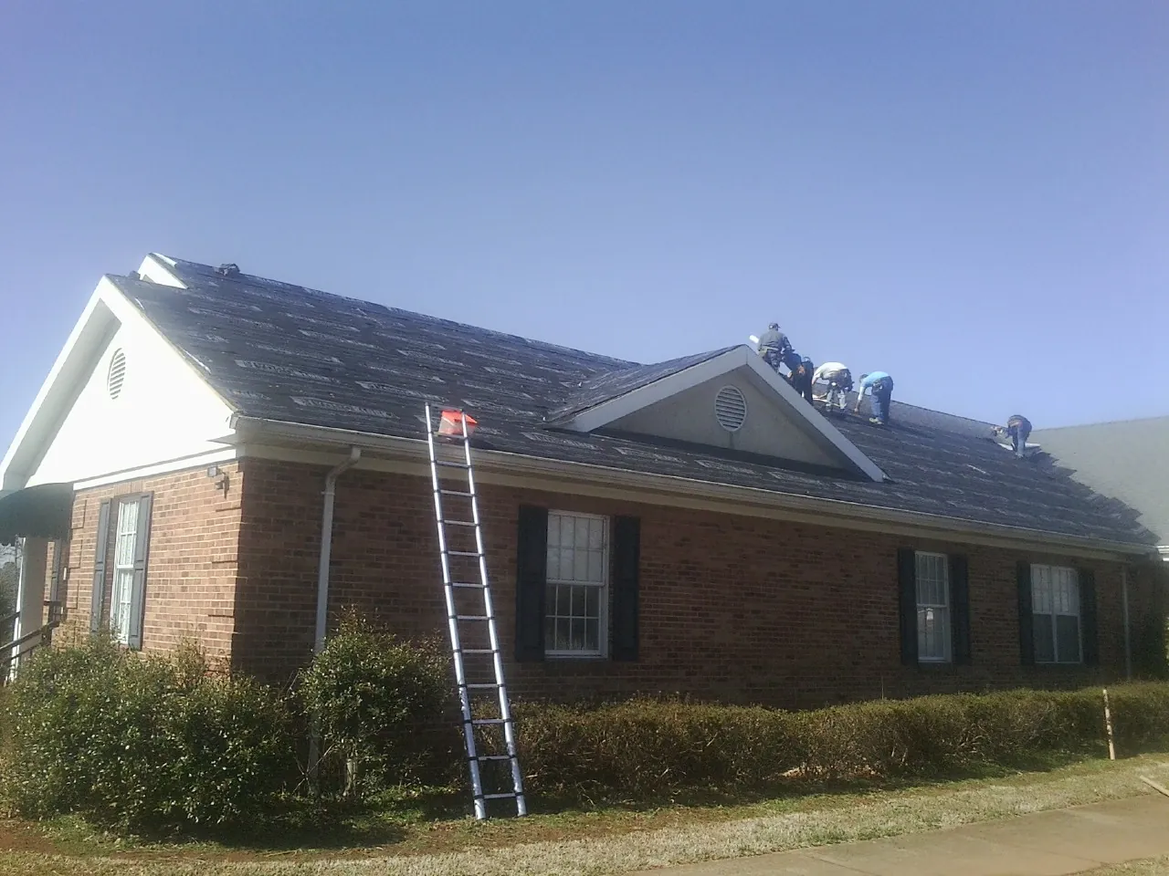 Crew tearing shingles off a brick ranch roof with a ladder set — Emergency Roof Repair work by our crew in Outlook