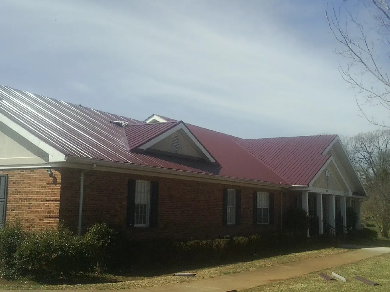 Red metal roof with gabled entries on a long brick building, from a Hail Damage Roof Repair job in Outlook