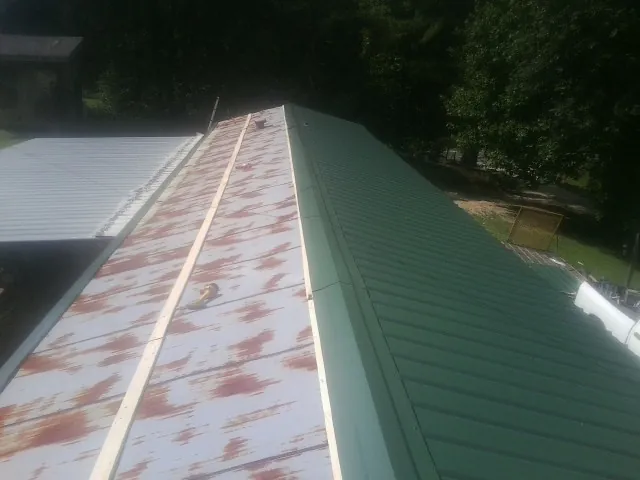 Old rusted panels beside newly installed green metal roofing — Wind Damage Roof Repair by Roofing Brothers in Outlook