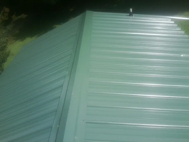 New green metal panels meeting at the ridge of a roof — Flat Roof Repair work by our crew in Outlook