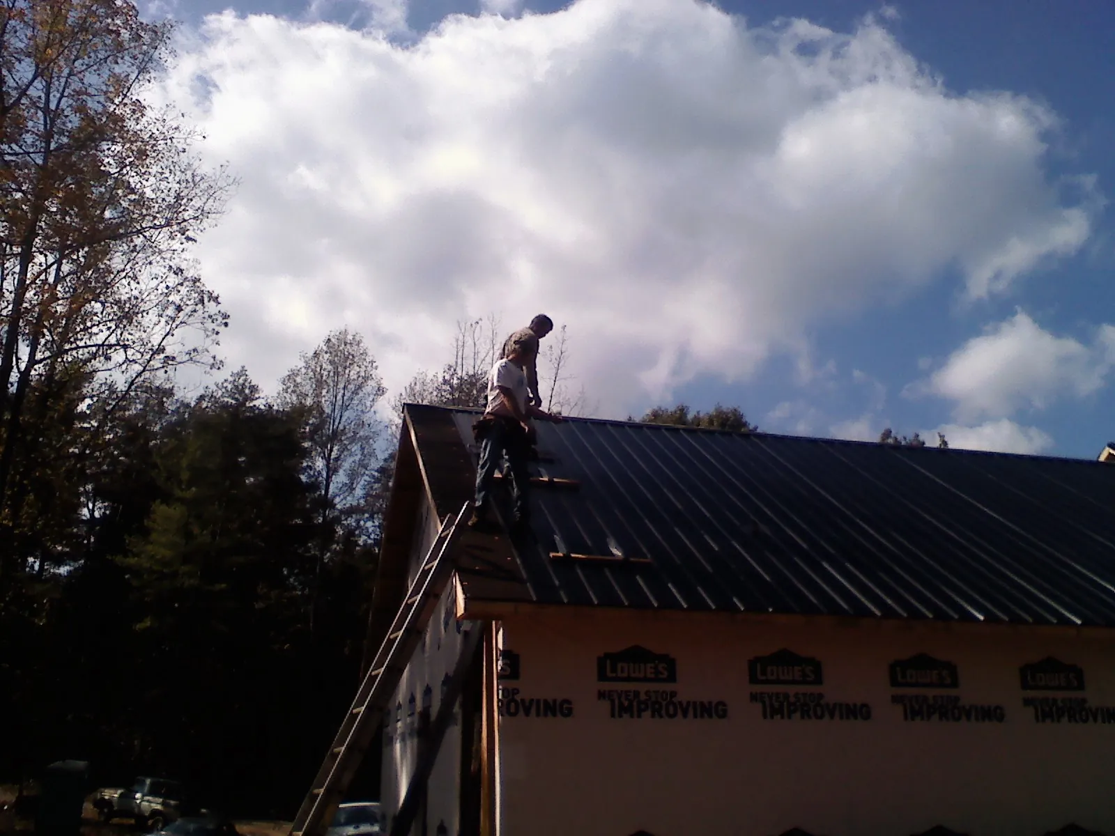 Roofer fastening dark metal panels high against a cloudy sky, from a Roof Inspection job in Outlook