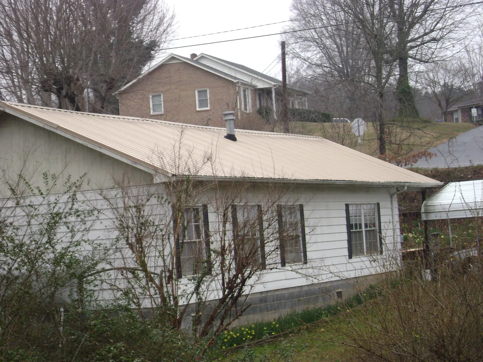 Tan metal roof on a white sided house set into a hillside — Commercial Roofing by Roofing Brothers in Outlook