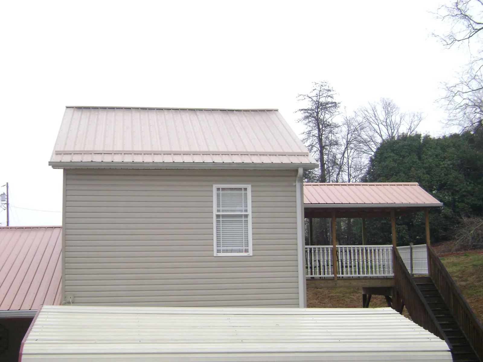 Tan metal roofs on a two story addition and attached porch, from a Roof Replacement job in Outlook